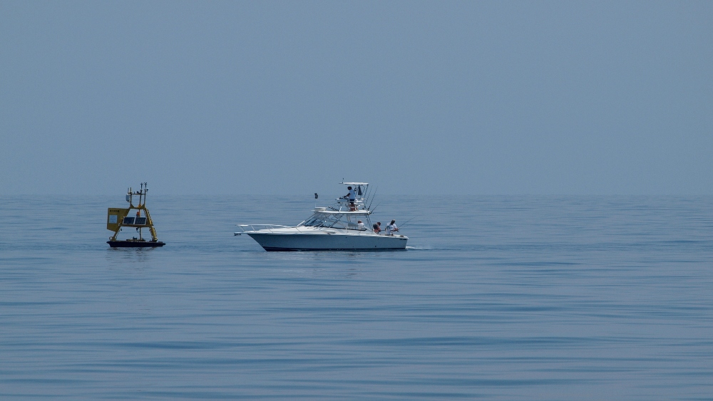 A boat fishing next to a yellow ocean buoy.