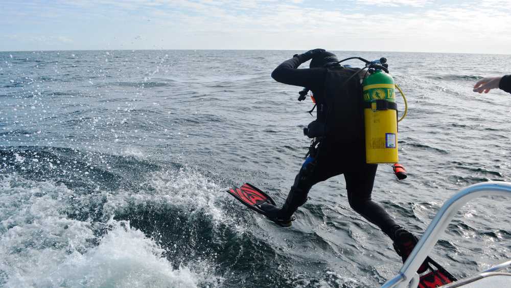 A scuba diver takes a giant stride to begin a dive in the ocean.
