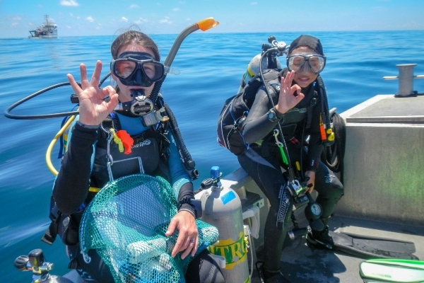 Two scuba divers sit on the gunwale of a boat on the ocean indicating they're ready to dive.