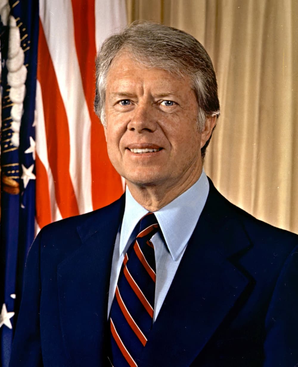 A portrait of a person in a blue suit in front of an American flag.