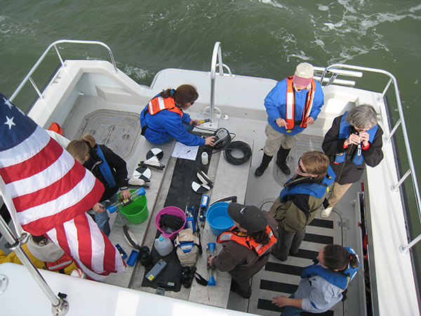 A group of people prepare scientific equipment on the deck of a boat.