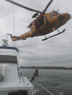 A Canadian rescue swimmer ropes from a Canadian Air Force Super Huey helicopter down to the deck of the R/V Joe Ferguson