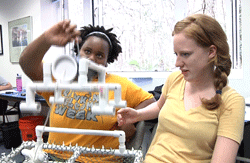 Tracy Wangui (l) and Amanda Hipp (r), demonstrate a prop they helped construct for an upcoming underwater robotics competition. 